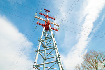 the support of a high-voltage power line is red and white against a blue sky view from below.