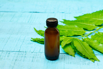 neem oil in bottle and neem leaf on blue wooden background.