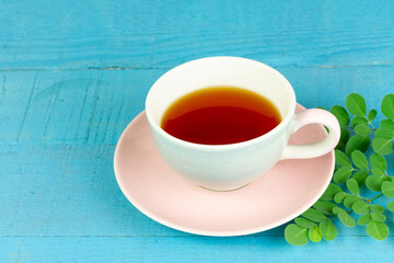 moringa tea in white ceramic cup and fresh green moringa leaf on blue wooden background. alternative healthcare and medical concept.