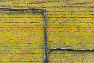 Electrical power cable wiring on old dirty green moldy brick wall facade background moss texture