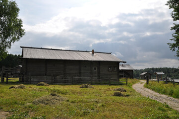 Fototapeta na wymiar Panoramic view of an old wooden house made of logs, a fence made of timber, a meadow with grass and wooden buildings. 03 August 2020, Arkhangelsk, Russia.