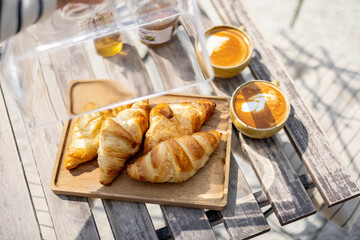 Croissants under the glass cloche with cups of coffee on the garden table. French style. Spend and enjoy time outdoors in the sun. 