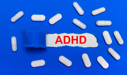 White pills lie on a beautiful blue background. In the center is white paper with the inscription ADHD. Medical concept. View from above.