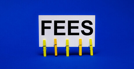 On a bright blue background on yellow clothespins, a white card with the text FEES