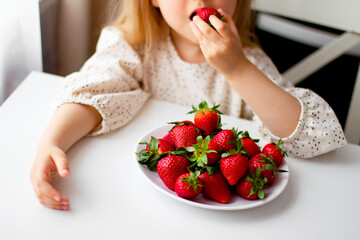 Cute little girl eating fresh strawberry in the kitchen. Healthy vitamin snack for kids. Ripe fresh berries. Harvest season. Natural vitamins .