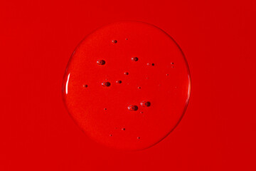 Clear transparent liquid gel drop or smear isolated on vivid red background. Top view. Virus protection or cosmetics concept. Serum texture
