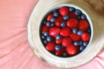 Bowl of blueberries and strawberries and wooden tray on a bed. Flat lay.