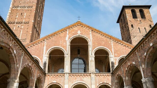 Facade of the famous romanic Sant'Ambrogio cathedral, Milan, Italy, point of interest for religion. Facade, with blue sky and clouds on the background; colonnade on either side. Time lapse.