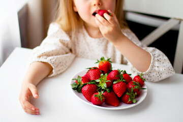 Cute little girl eating fresh strawberry in the kitchen. Healthy vitamin snack for kids. Ripe fresh berries. Harvest season. Natural vitamins .