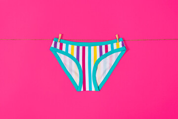 Womens colorful striped panties hang on a rope. Girls underpants isolated on pink background