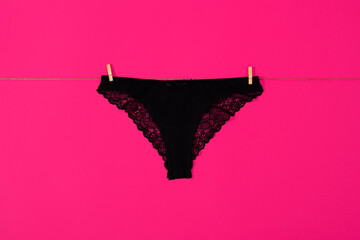 Womens black lace panties hanging on a rope. Girls underpants isolated on pink background