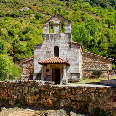 Fototapeta na wymiar Small stone chapel next to ancient stone wall in the green field. Asturias Spain.