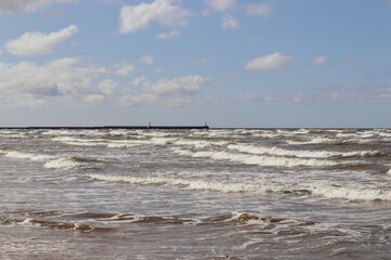 Sea waves under blue clody skies with pier in the distance