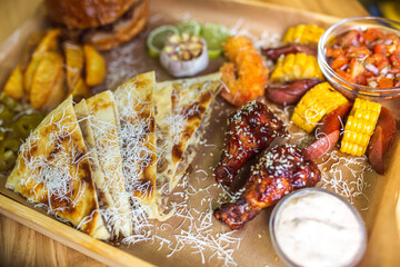 Food set of fried chicken wings, burger, fried potatoes, cheese, corn, sauce, salad