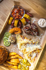 Food set of fried chicken wings, burger, fried potatoes, cheese, corn, sauce, salad