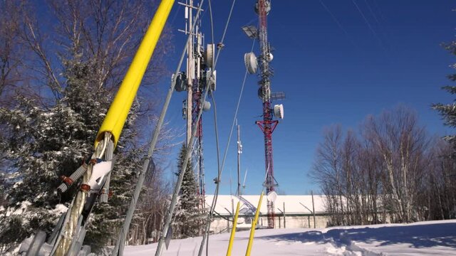Tilting up and panning video of tall towers and cables for communication situated in a snowy area, surrounded by bare pine trees. 