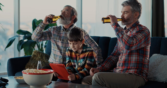 Boy teenage son playing videogame on smartphone in circle of family. Excited grandfather and daddy watching on screen supporting the child.