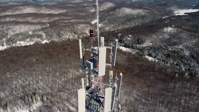 Drone videography showing the top of state of art 4G and 5G cellular signals transmittal tower with wires and antennas, with snow in the surrounding.