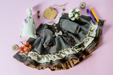 Dress for a doll with sewing tools on a pink background.