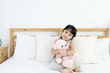 Adorable happy Asian toddler girl sitting in bed with smiling face and her teddy bear