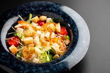 Fresh caesar salad with grilled chicken in a served plate on a black background.
