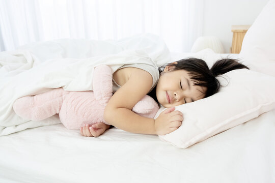 Portrait of a little girl sleeping in bed with a pink teddy bear at home
