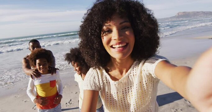 Smiling african american parents and their children taking a selfie with smartphone on the beach