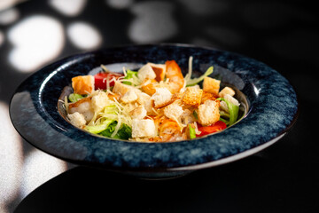 Fresh caesar salad with grilled chicken in a served plate on a black background.
