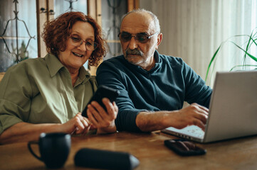 Senior couple using a smartphone and a laptop