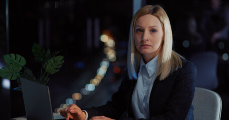 Young adult blonde woman using laptop working on deadline presentation project staying long in the office. Workaholic people.