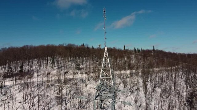 An exciting drone video featuring tall cellular communication towers for signal transmitters, located in snowy areas, surrounded by bare trees.