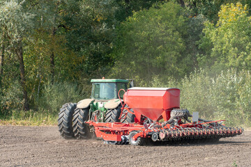 Fototapeta premium Sowing equipment works on the field on a dry summer day. Season to sow cereals. A farmer driving a tractor with a cultivator.