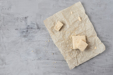 Peanut halva lying on parchment paper on a gray background. Top view, copy space. Traditional national dessert. Turkish, Arabic, Oriental cuisine.