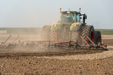 Fototapeta premium A large tractor with a plow is working in the field. Tillage before sowing. Loosening and plowing the soil before planting wheat and other cereals. Agricultural work.