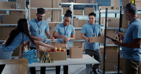 Group of multi-ethnic volunteers in blue uniform gathering and collecting boxes with food delivery for edlerly people during covid-19 pandemic.