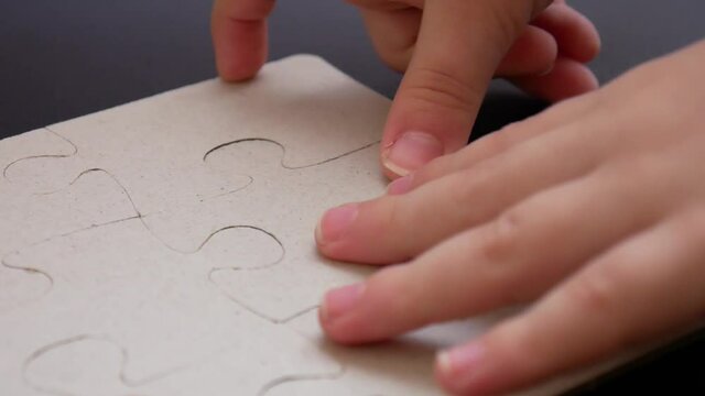 A childs hands substitute the missing cardboard puzzle on black leather surface close-up