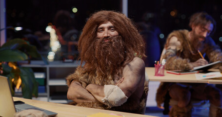 Portrait of Savage Neanderthal Tribesman Sitting in Office Doing Modern Work on Computer Learning Technology Posing for Camera. Homo Sapiens. Evolution.