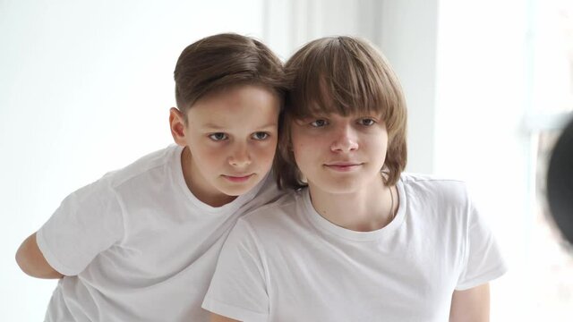 two boys in white T-shirts pose for a photographer in a photo studio.