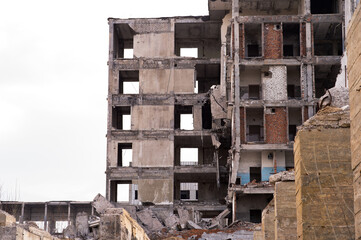 A ruined building against a cloudy gray sky with large foundation piles in the foreground. Background