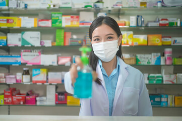 Portrait of asian woman pharmacist wearing a surgical mask using alcohol gel in a modern pharmacy drugstore, covid-19 and pandemic concept.