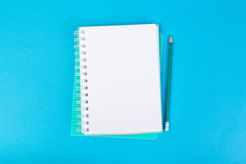 school notebooks on a blue background, spiral notepad with a blank page and a pencil on the table top view