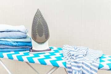 Electric iron on the ironing board and a pile of colorful clothes stacked on the ironing board