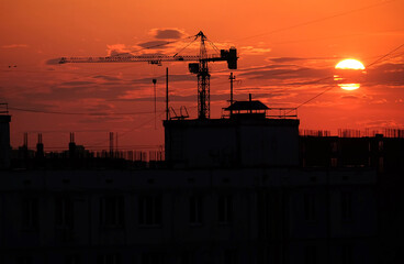 Contour of tower crane above the constructing buildings against evening sky and the red beautiful sunset with some clouds