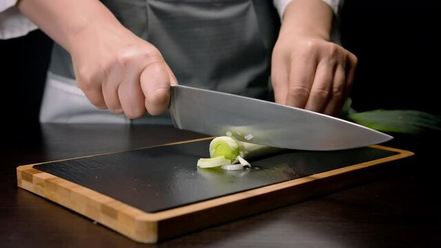 Female hands chopping leek with kitchen knife on cutting board. Close up
