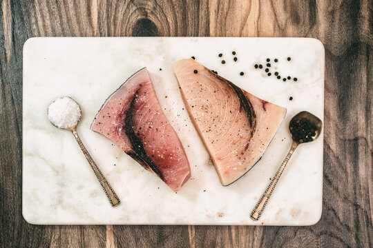 Raw swordfish. Two pieces of fresh raw fish steaks with salt and black pepper close up on marble cutting board on wooden background