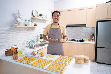 proud asian young man with his cooking smiling to camera. making nastar cake for eid mubarak at home. small business owner with his product