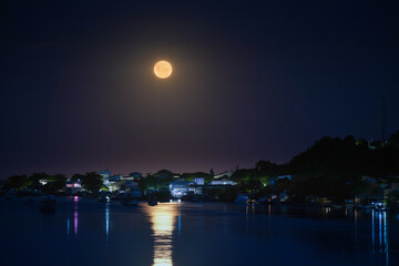 Full moon over riverside city. Relection of light on water. Orange moon in a beautiful night....