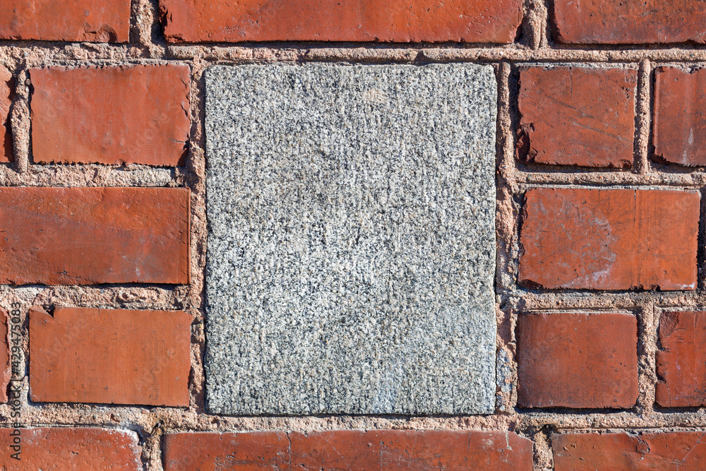 Aufkleber on a stone wall of red brick in the middle of a square of gray granite