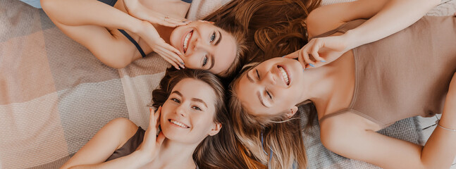 Women rest and have fun. Girlfriends laugh at home lying on the floor on pillows. Tree girls make homemade face and hair beauty masks. Women take care of youthful skin.