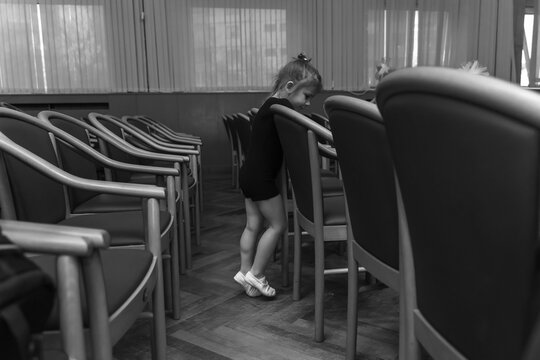 a little girl in a black gymnastic suit and white toe shoes stands alone in an empty auditorium. black and white photo